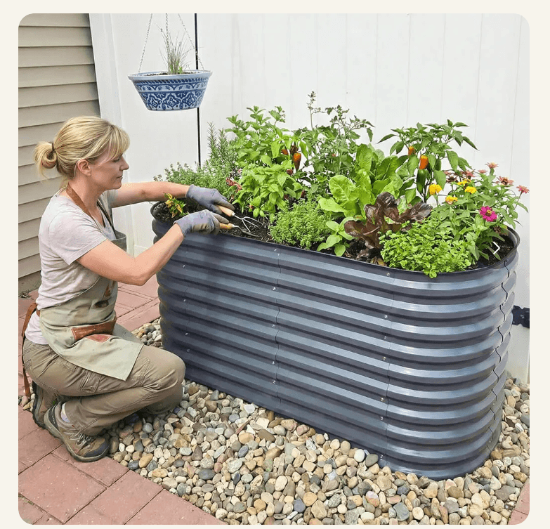 Woman kneeling beside a dark gray Vegega 32 inch raised garden bed on a gravel patio, planting herbs and flowers